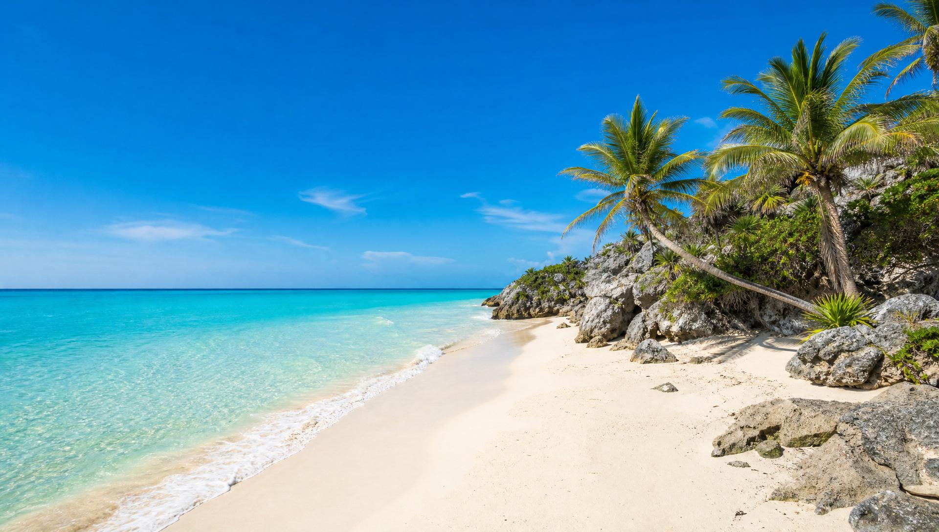 Bright sunny Tulum-style Mexican beach with turquoise Caribbean water, white sand, and palm trees and rocks on the right